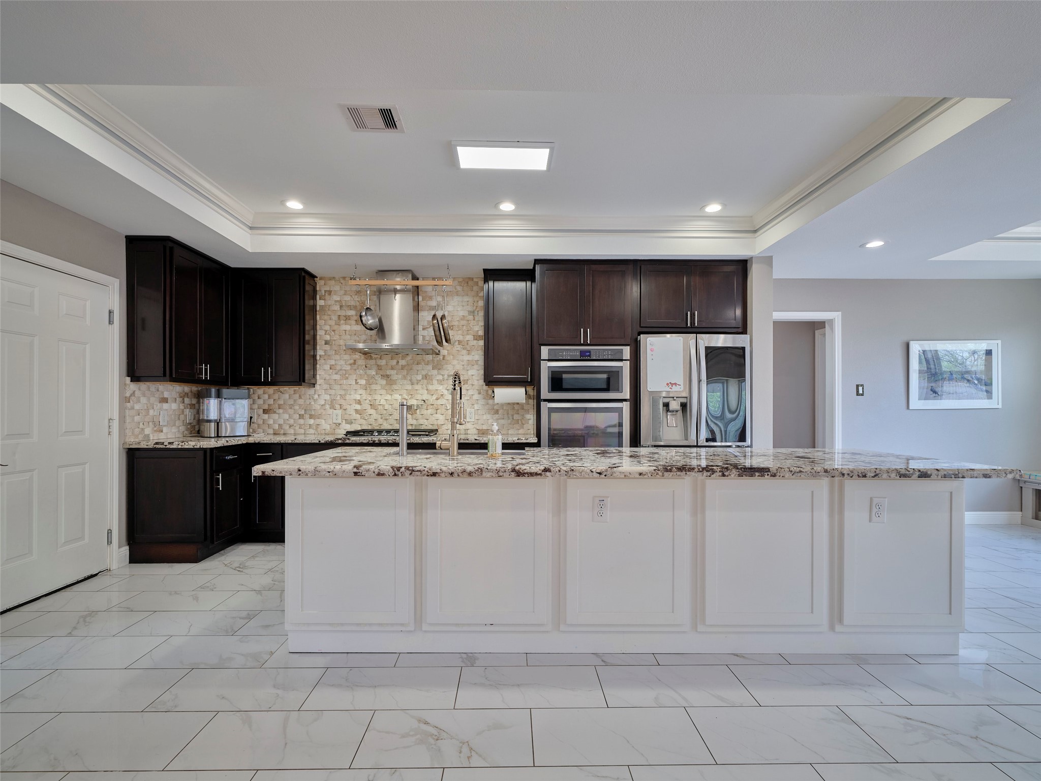 4219 Redbud Street Houston, TX 77051 - Photo 8 of 25 This modern kitchen features elegant dark wood cabinets, stainless steel appliances, and a spacious marble island. The open layout is highlighted by a tiled floor and recessed lighting, creating a bright and inviting space.