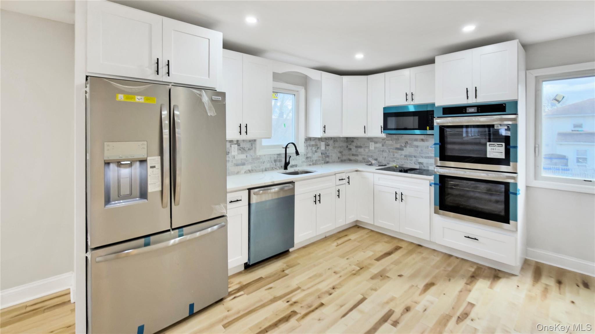 37 Deal Road Island Park, NY 11558 - Photo 16 of 50 Kitchen with appliances with stainless steel finishes, white cabinetry, tasteful backsplash, light wood finished floors, and recessed lighting