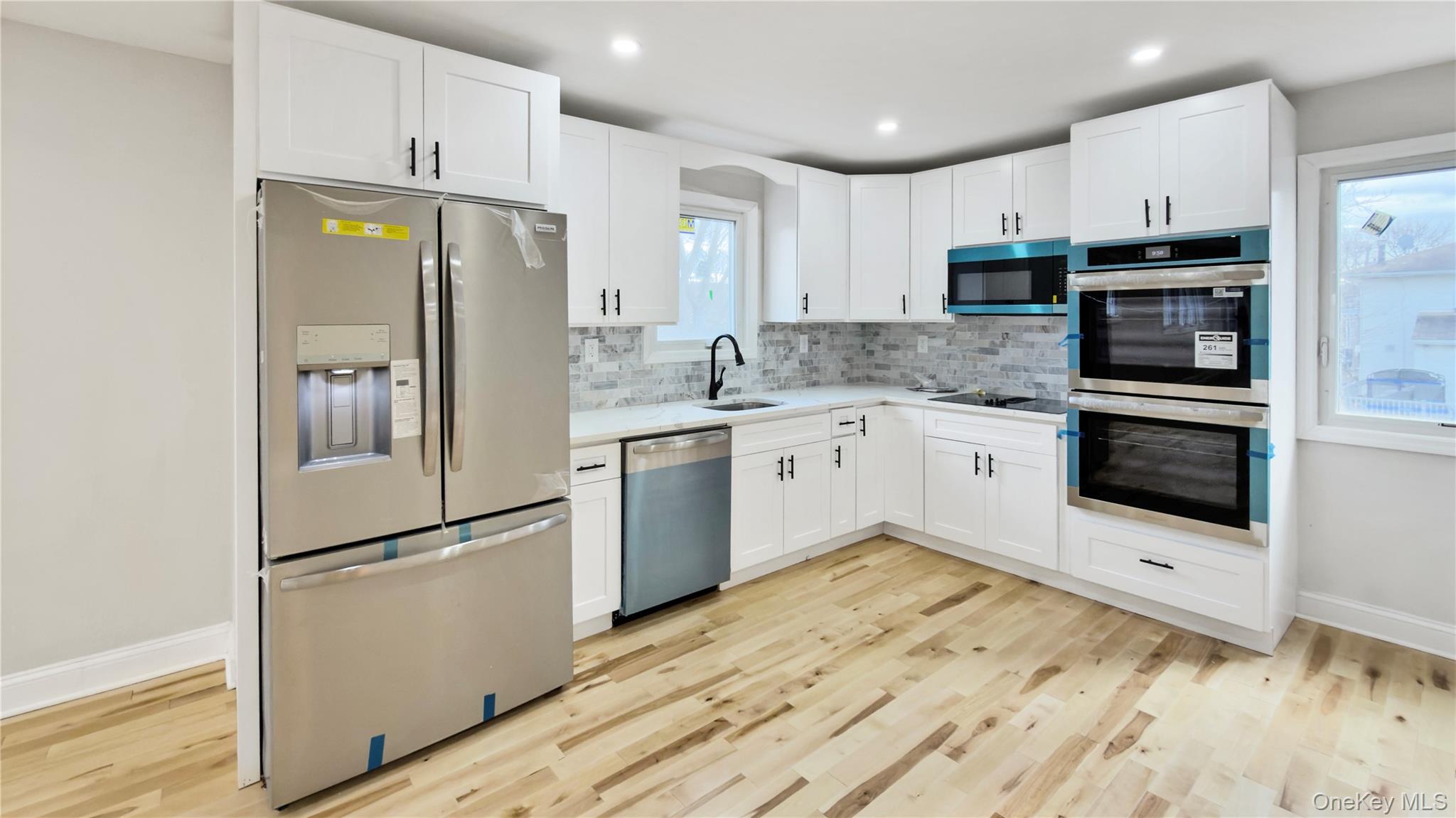 37 Deal Road Island Park, NY 11558 - Photo 17 of 50 Kitchen featuring appliances with stainless steel finishes, white cabinetry, backsplash, light wood finished floors, and recessed lighting
