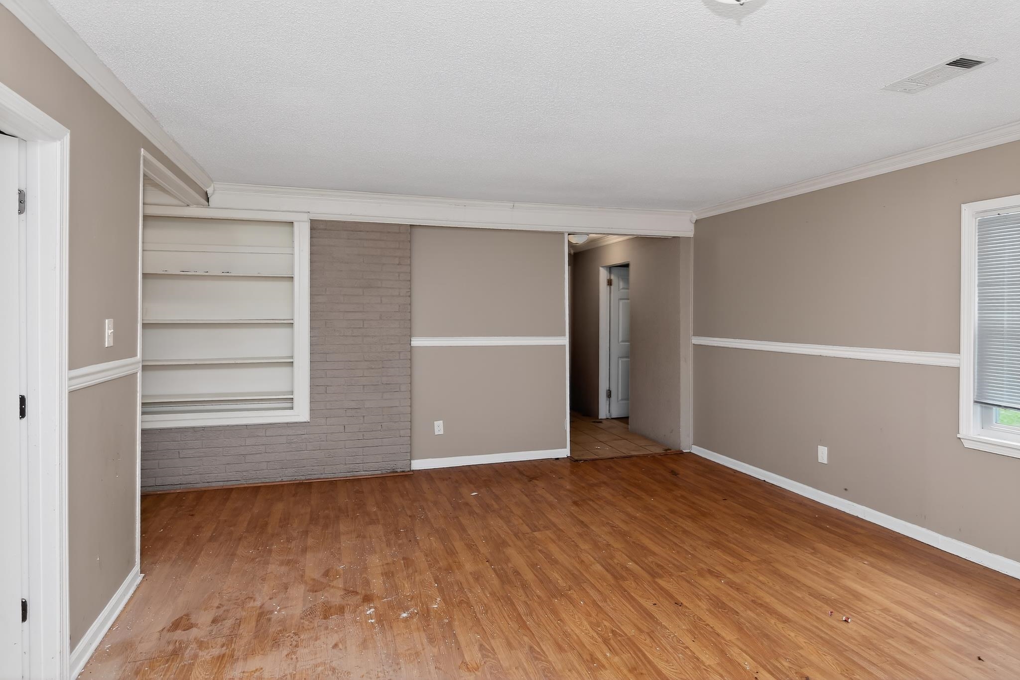 1403 Old Hickory Road Memphis, TN 38116 - Photo 8 of 31 Spacious room featuring wood-finish flooring, neutral-toned walls with chair rail molding, built-in shelving, and a painted brick accent wall