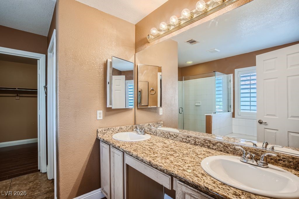 591 Fox Chase Street Henderson, NV 89015 - Photo 12 of 22 Bathroom featuring a textured wall, a spacious closet, double vanity, a stall shower, and a garden tub