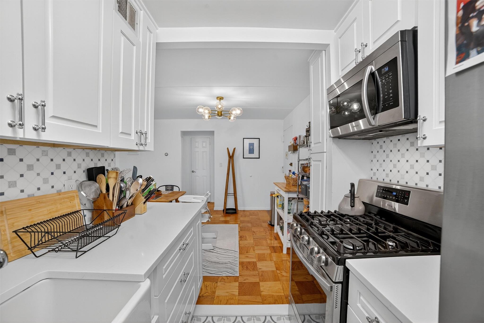 108 Sagamore Road, Unit 5F Tuckahoe, NY 10707 - Photo 23 of 33 Kitchen with stainless steel appliances, white cabinets, light countertops, backsplash, and a chandelier