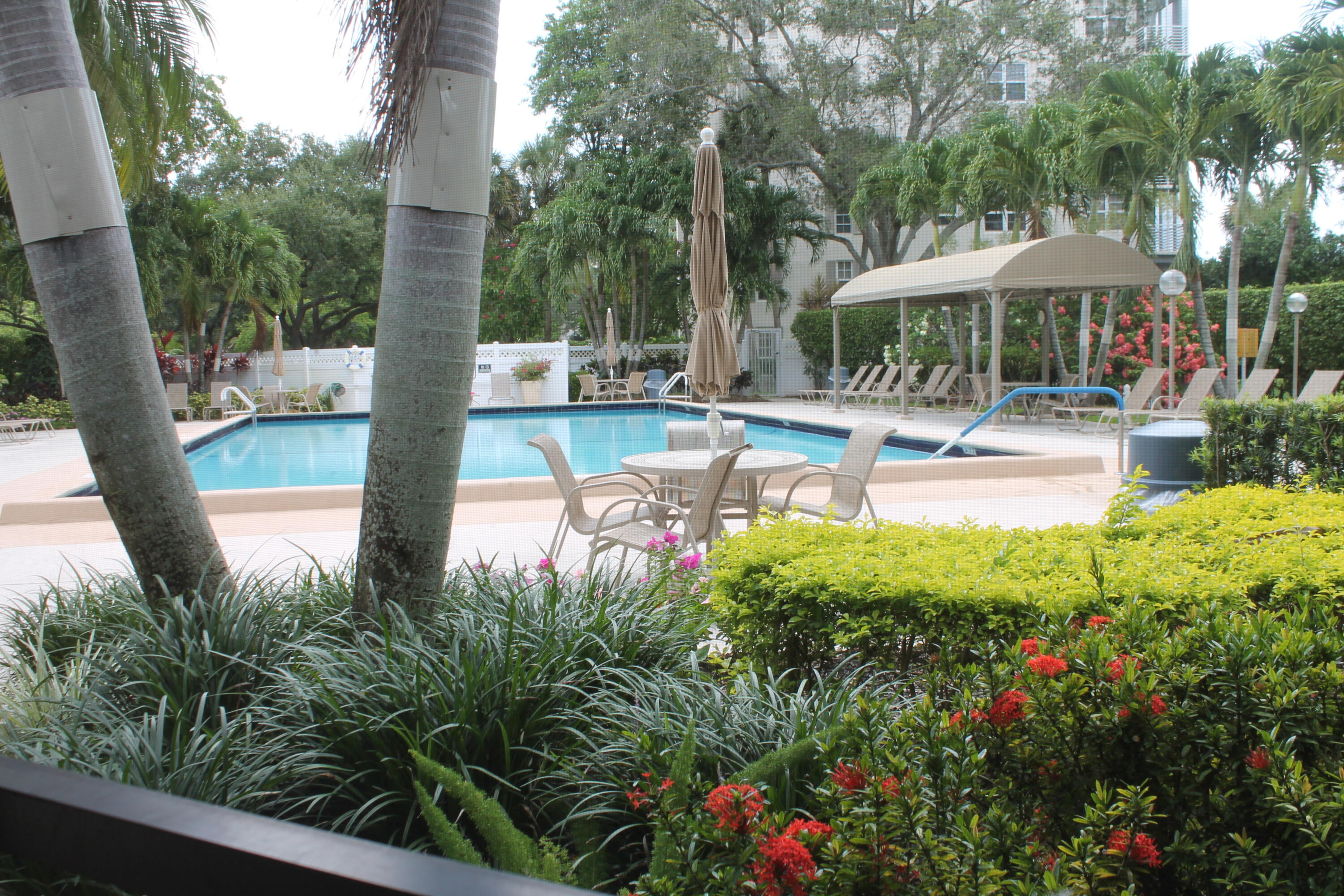 3520 Oaks Way, Unit 607 Pompano Beach, FL 33069 - Photo 44 of 46 a view of a patio with chairs and a table and chairs under an umbrella with large trees