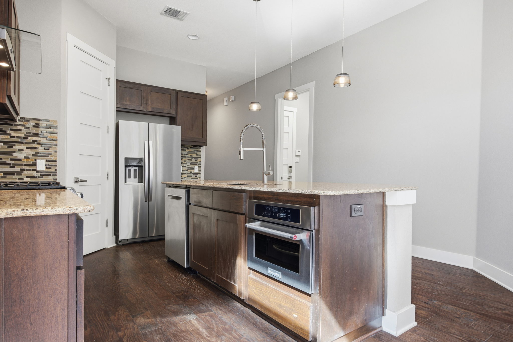 3521 Marcae Court Austin, TX 78704 - Photo 12 of 37 Kitchen with a center island with sink, dark wood finish cabinets, dark wood-type flooring, stainless steel appliances, and light stone countertops