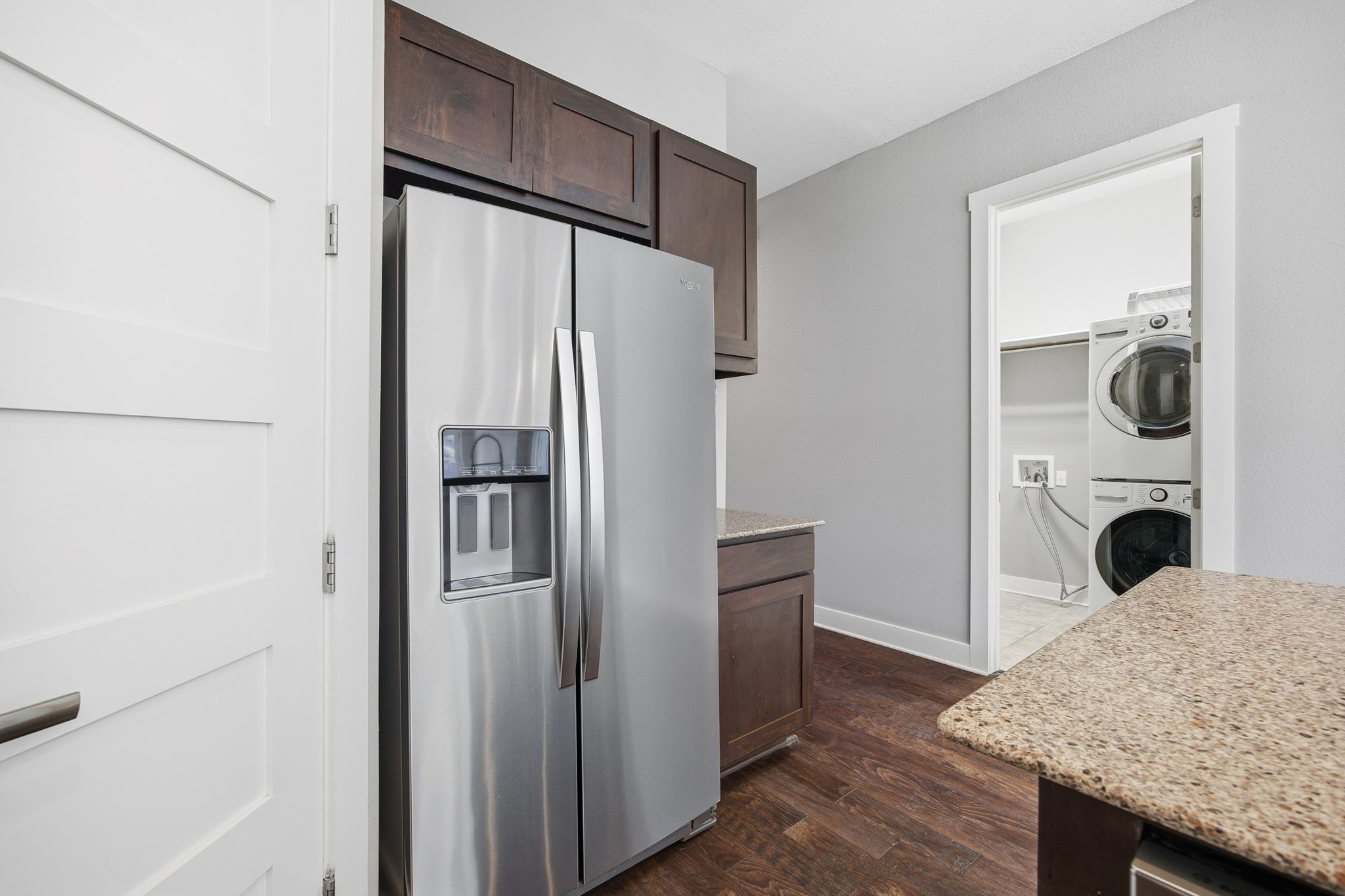 3521 Marcae Court Austin, TX 78704 - Photo 13 of 37 Kitchen featuring stainless steel fridge, dark wood-style flooring, dark wood finish cabinets, light stone counters, and stacked washer / dryer