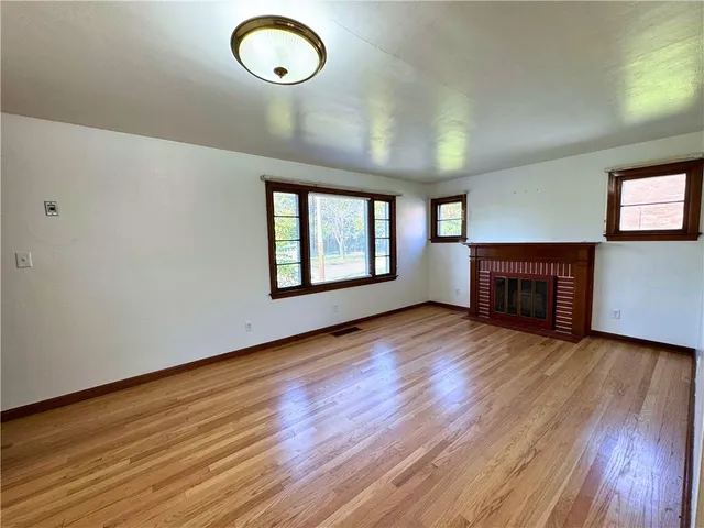 an empty room with wooden floor fireplace and windows