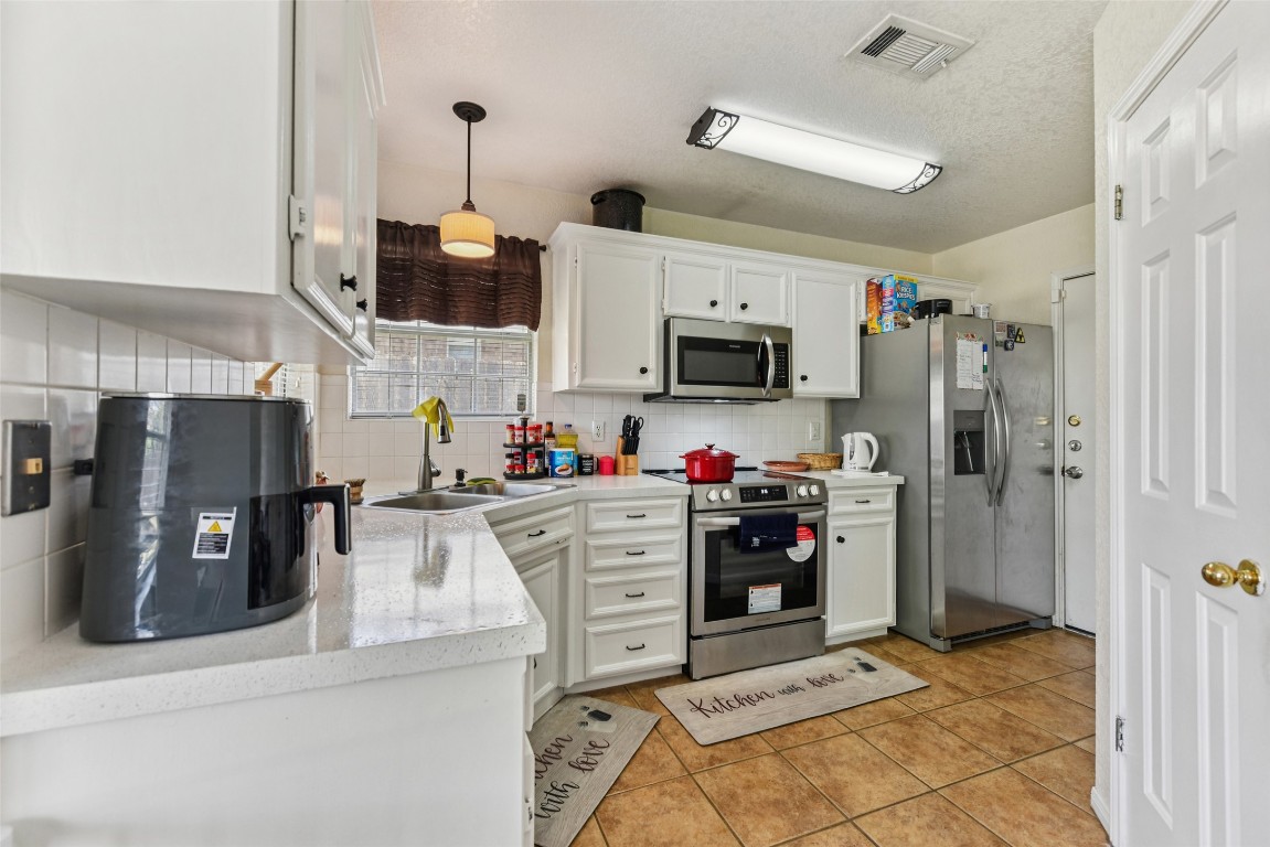 5318 West Ridge Boulevard Temple, TX 76502 - Photo 9 of 27 Kitchen featuring light countertops, backsplash, white cabinets, appliances with stainless steel finishes, and light tile patterned flooring