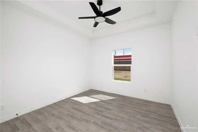 an empty room with wooden floor ceiling fan and windows
