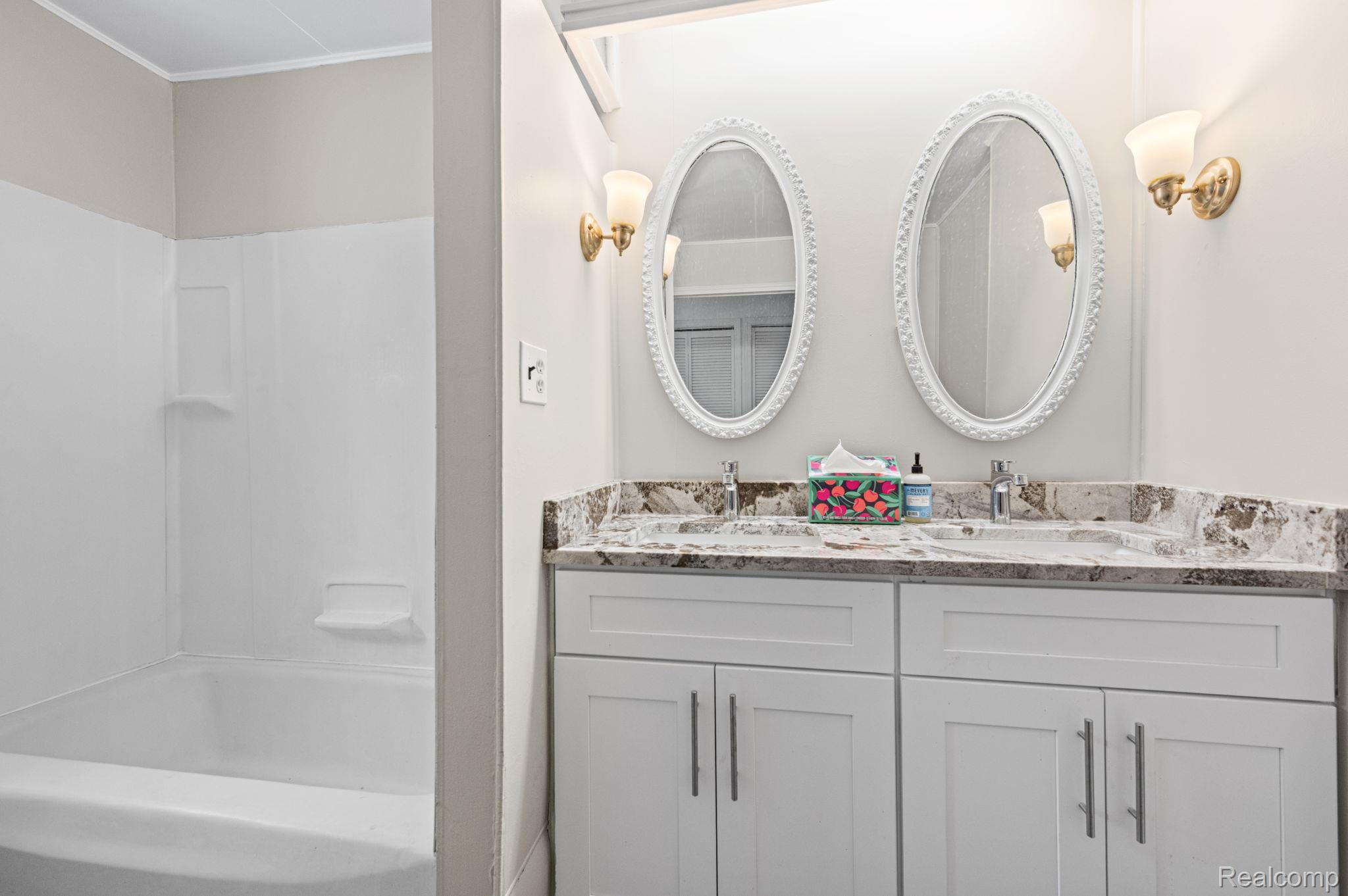 7993 Church Road Grosse Ile, MI 48138 - Photo 17 of 37 Dual vanity with white cabinetry and stone countertop featuring two oval mirrors and brass-toned wall sconces