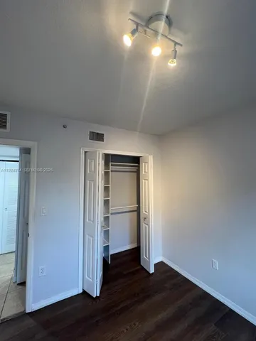 an empty room with wooden floor closet and windows