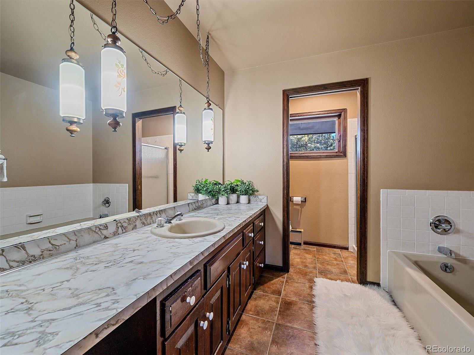 7990 Tim Tam Trail Evergreen, CO 80439 - Photo 22 of 45 a spacious bathroom with a granite countertop double vanity sink a mirror and a bathtub