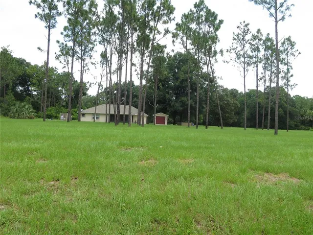 a view of a white house with a big yard and large trees
