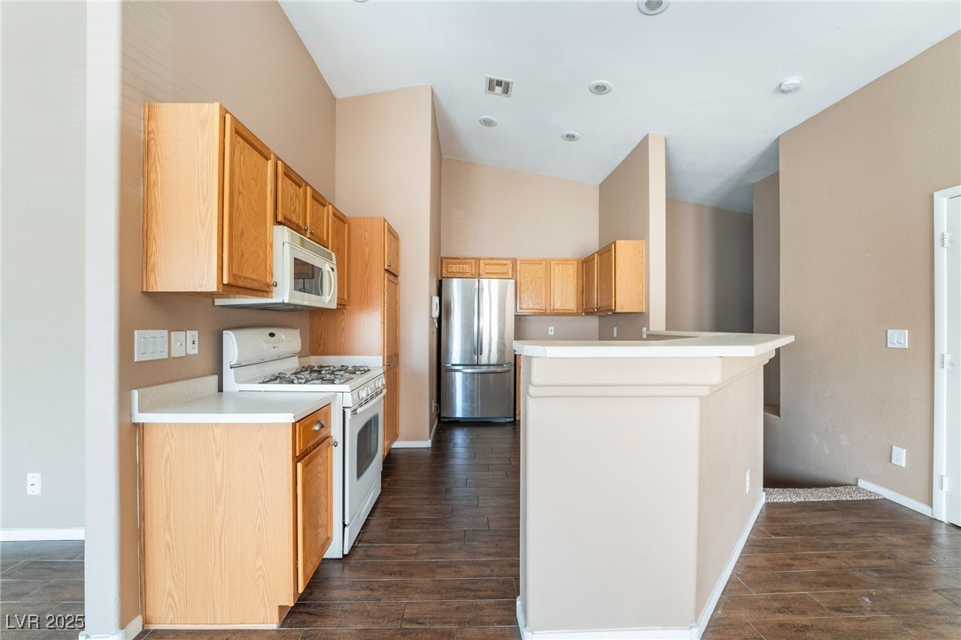 1570 Rusty Ridge Lane Henderson, NV 89002 - Photo 20 of 35 Kitchen with baseboards, white appliances, a peninsula, light countertops, and dark wood-type flooring