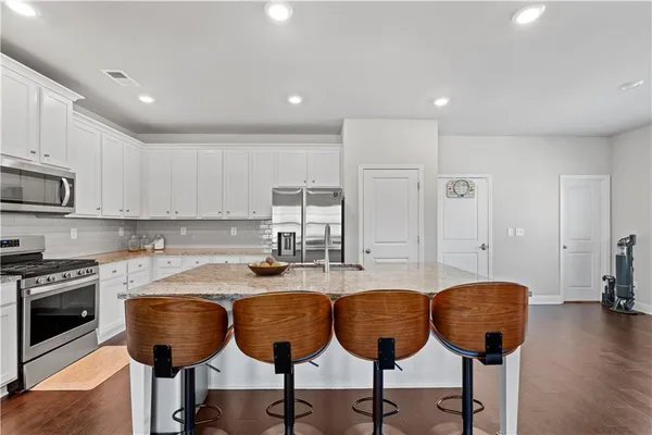 a kitchen with stainless steel appliances granite countertop a stove a sink a refrigerator and white cabinets with wooden floor