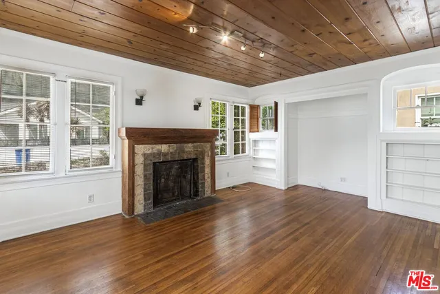 a view of an empty room with wooden floor fireplace and a window