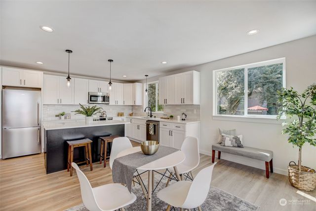 a kitchen with stainless steel appliances kitchen island granite countertop a refrigerator a stove a sink a dining table and chairs with wooden floor