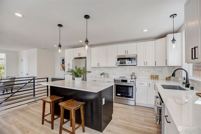 a kitchen with stainless steel appliances a sink a stove a refrigerator white cabinets and wooden floor