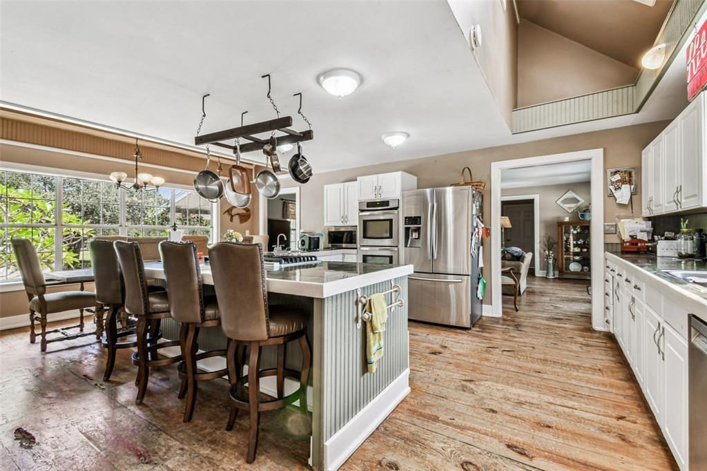 15019 Carlton Lake Road Wimauma, FL 33598 - Photo 14 of 89 an open kitchen with stainless steel appliances kitchen island granite countertop a refrigerator a stove a dining table and chairs with wooden floor