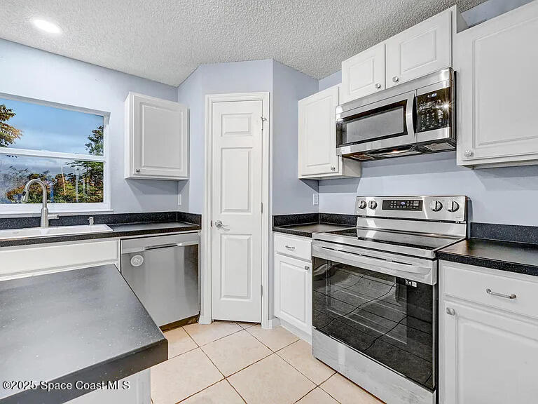 2240 Spring Creek Circle Palm Bay, FL 32905 - Photo 11 of 29 a kitchen with stainless steel appliances white cabinets a stove a sink and a microwave