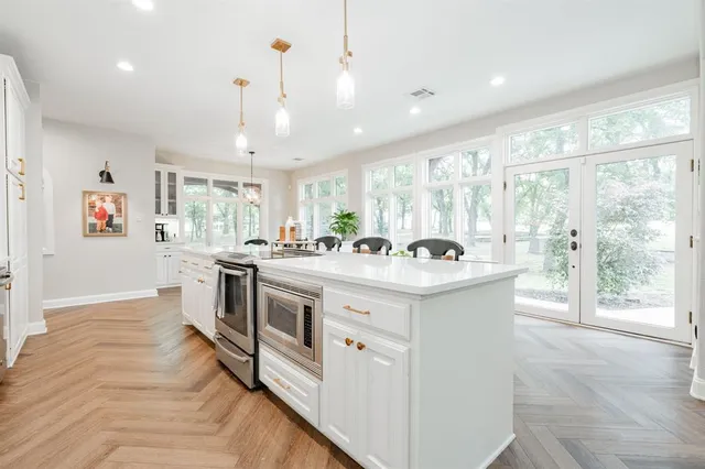 a large white kitchen with kitchen island a large counter top space a sink stainless steel appliances and cabinets