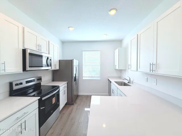 a kitchen with stainless steel appliances a stove top oven a sink a refrigerator white cabinets and wooden floor