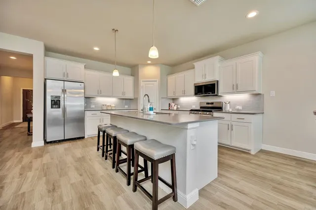 a kitchen with granite countertop a refrigerator stove a sink and white cabinets with wooden floor