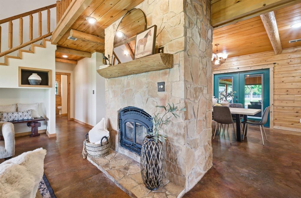 465 Emberson Ranch Road Pilot Point, TX 76258 - Photo 6 of 37 Stone fireplace with hearth, wood-finish flooring, natural wood ceiling, wood beam accents, and a wood staircase with a log railing