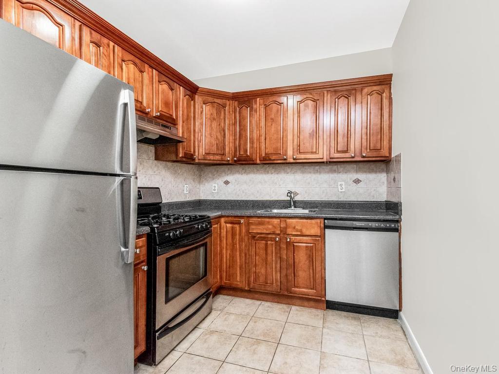 25 Trinity Place, Unit 3J New Rochelle, NY 10805 - Photo 2 of 15 Kitchen featuring wood cabinetry with crown molding, stainless steel appliances, a tile backsplash, and dark countertops