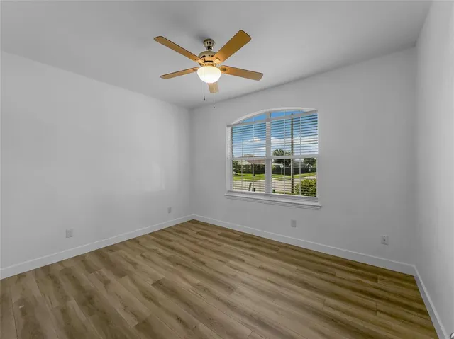 an empty room with wooden floor ceiling fan and windows