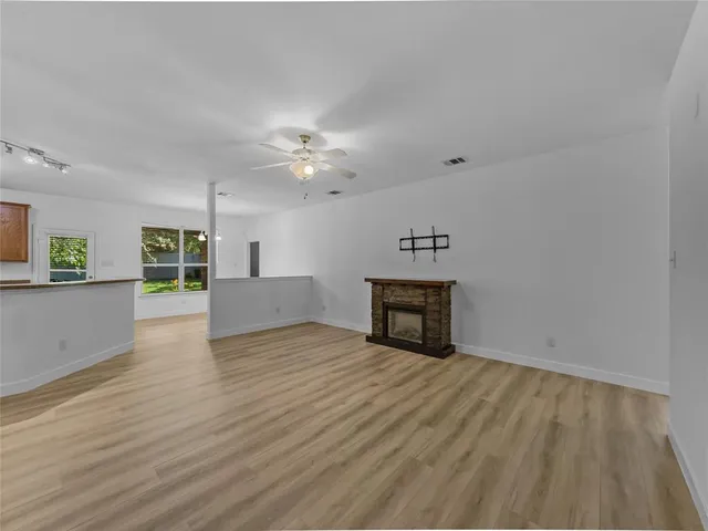 a view of an empty room with wooden floor and a kitchen