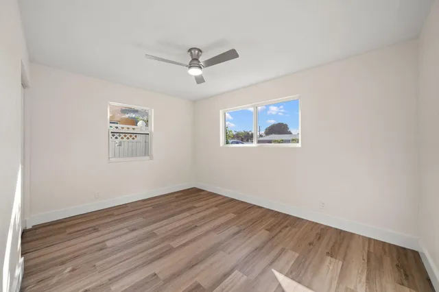 an empty room with wooden floor ceiling fan and windows