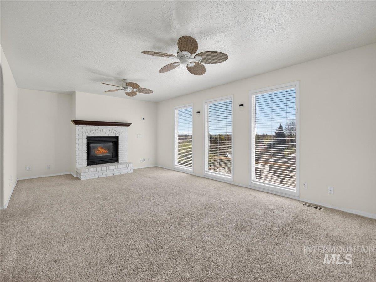 398 Pebble Beach Way Eagle, ID 83616 - Photo 11 of 35 Spacious living area featuring a white brick fireplace with a dark wood mantel, multiple large windows, and neutral carpeting