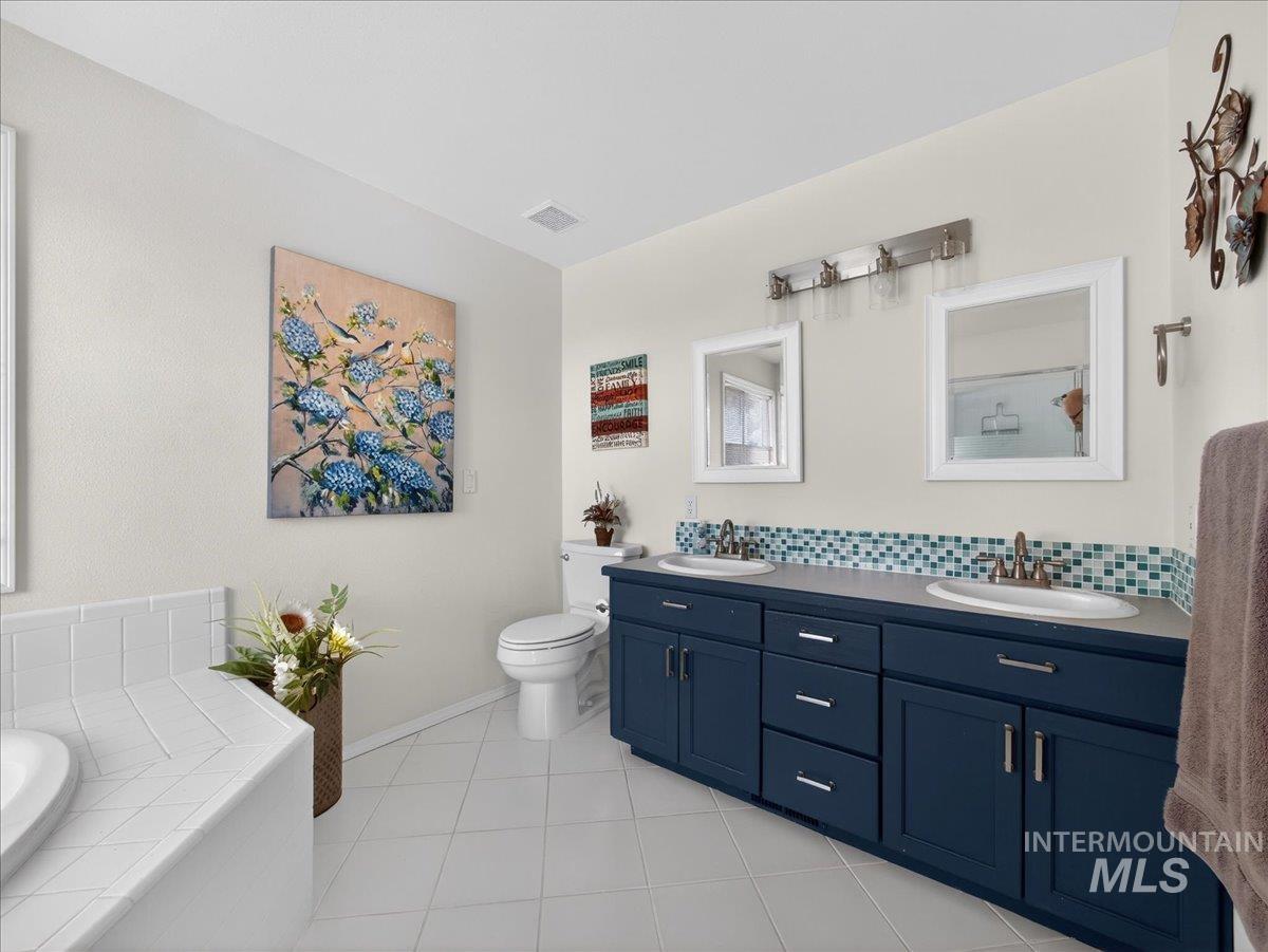 398 Pebble Beach Way Eagle, ID 83616 - Photo 18 of 35 Bathroom featuring a dual vanity with navy cabinetry, an integrated white bathtub, and white floor tiles