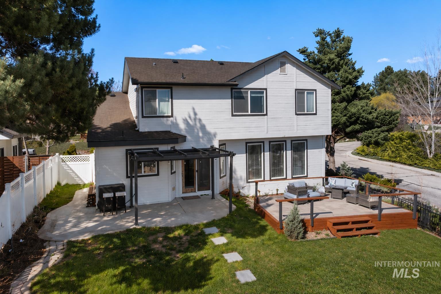 398 Pebble Beach Way Eagle, ID 83616 - Photo 29 of 35 Rear exterior featuring a two-story design with white siding and black trim, a wood deck with a dark railing system, a concrete patio with an overhead pergola structure, a green lawn, and mature trees