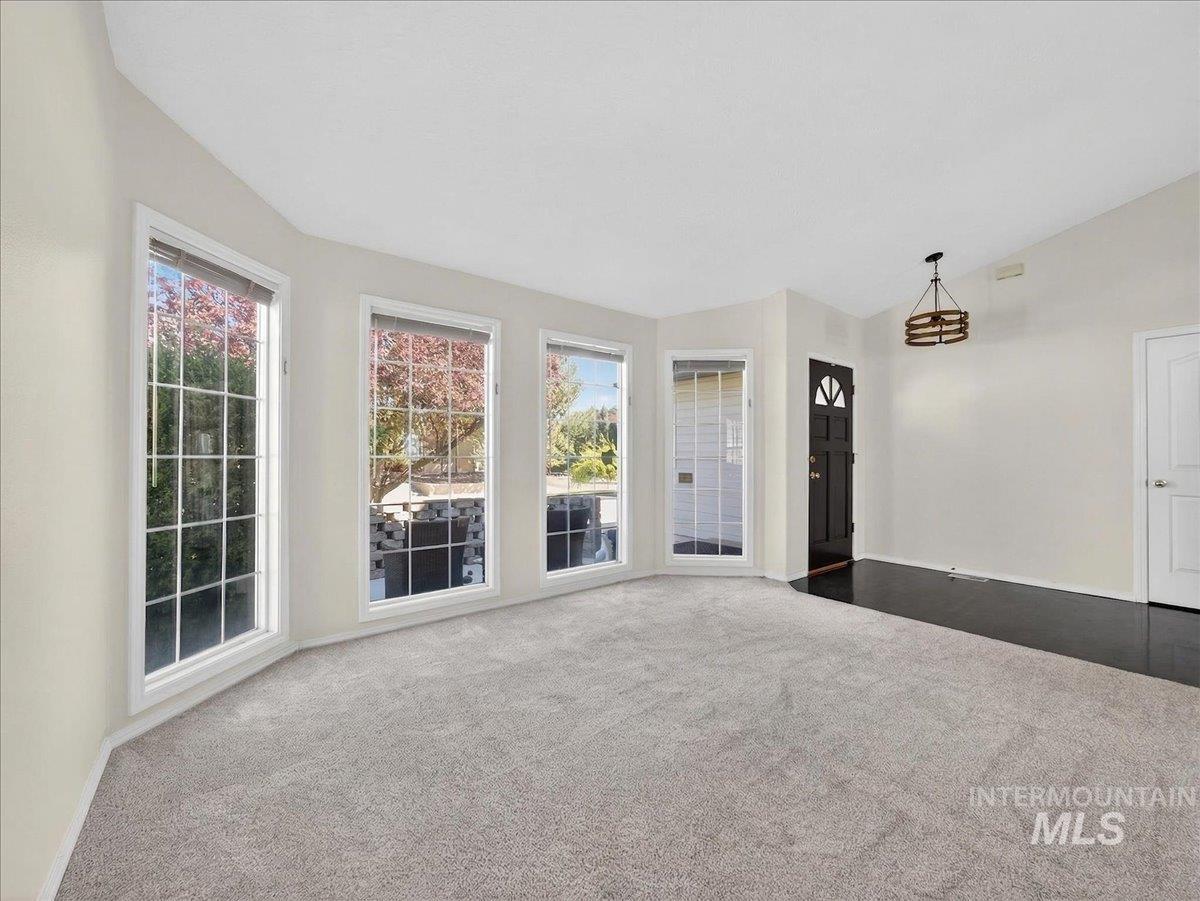 398 Pebble Beach Way Eagle, ID 83616 - Photo 5 of 35 Bay window with multiple panes, light gray carpeting, dark wood-finish flooring, black entry door with decorative glass, and a vaulted ceiling