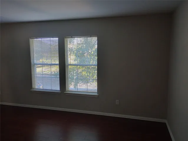 an empty room with wooden floor and windows with curtains