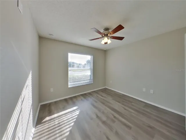 an empty room with wooden floor fan and windows
