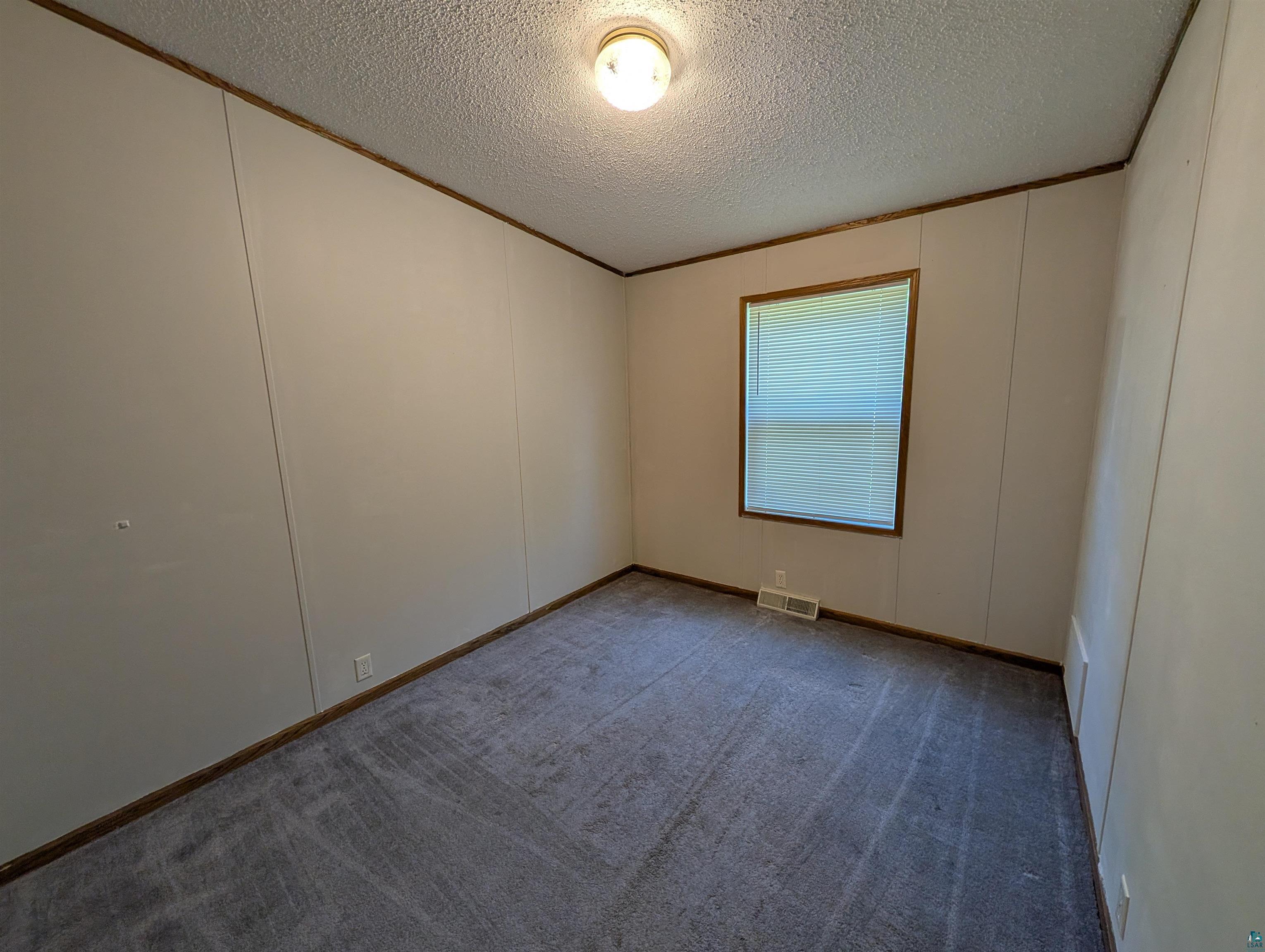 3945 Maple Street Kettle River, MN 55757 - Photo 22 of 41 Room featuring light-colored wall panels, wood-finish trim, a single window with blinds, and gray patterned carpeting