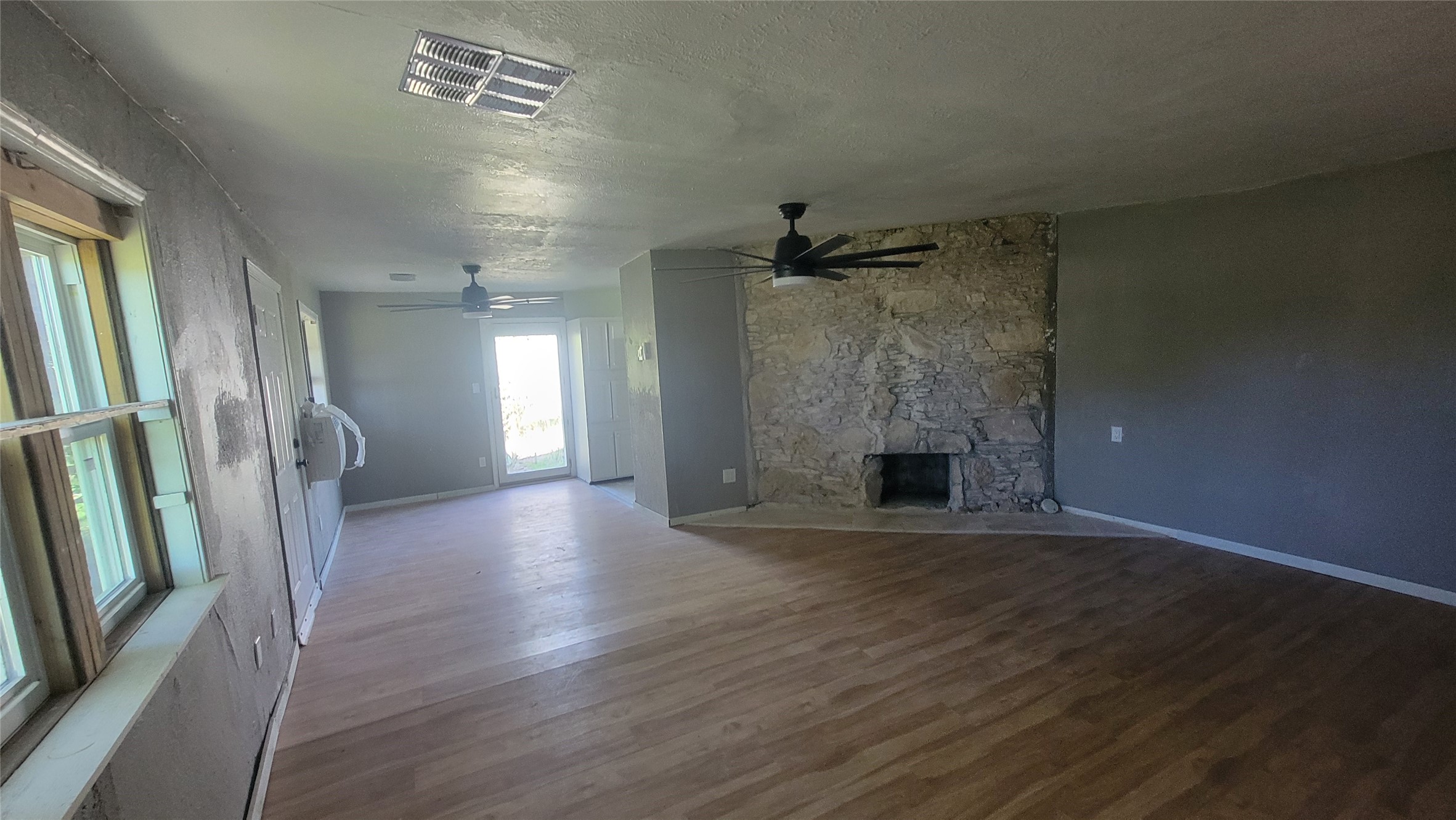 12018 Sandpiper Road Angleton, TX 77515 - Photo 31 of 48 This spacious living area features wood flooring, a stone fireplace, and ceiling fans. Large windows and a glass door provide plenty of natural light, creating an inviting atmosphere.