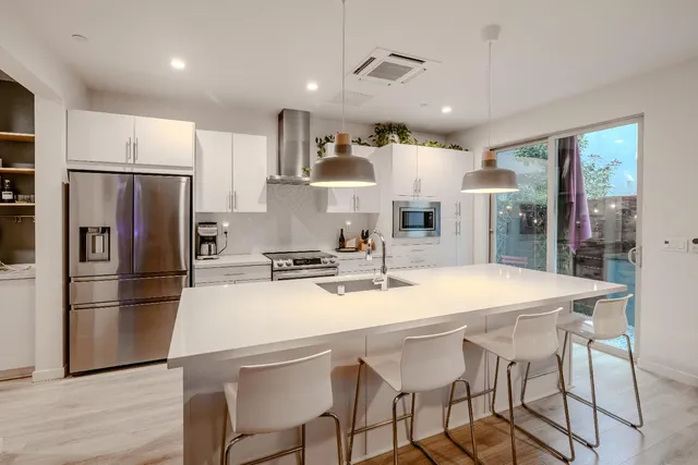 a kitchen with stainless steel appliances granite countertop a stove a refrigerator a sink dishwasher a dining table and chairs with wooden floor
