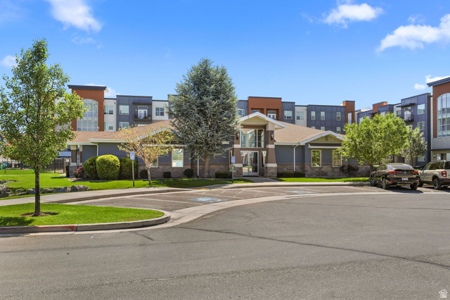 8264 South Resaca Drive, Unit K3 Sandy, UT 84070 - Photo 27 of 30 Modern multi-story building featuring a prominent central entrance with a glass facade, a mix of siding and stone veneer, and a paved parking area