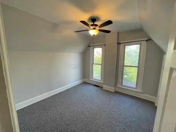 an empty room with a chandelier fan and windows