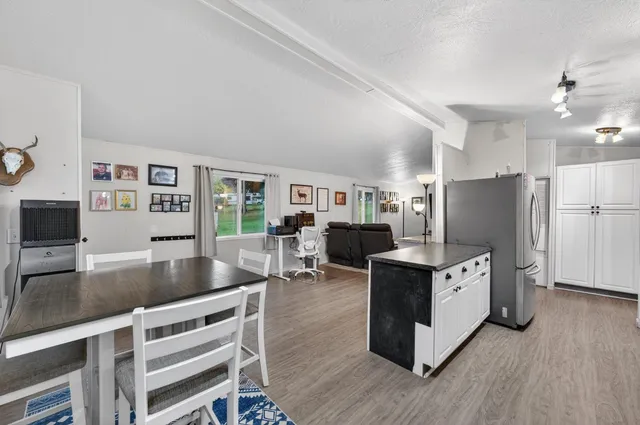 a living room with stainless steel appliances kitchen island granite countertop a table chairs and a refrigerator