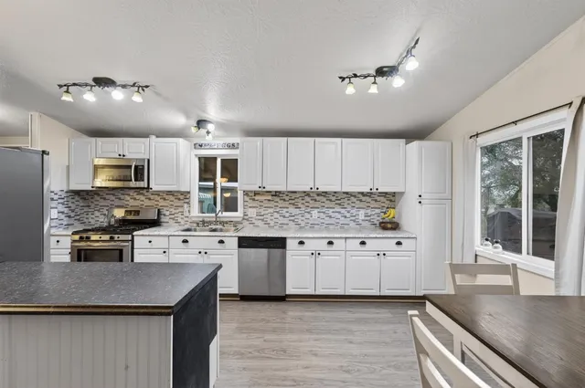 a kitchen with granite countertop a stove top oven a sink dishwasher a dining table and chairs with wooden floor