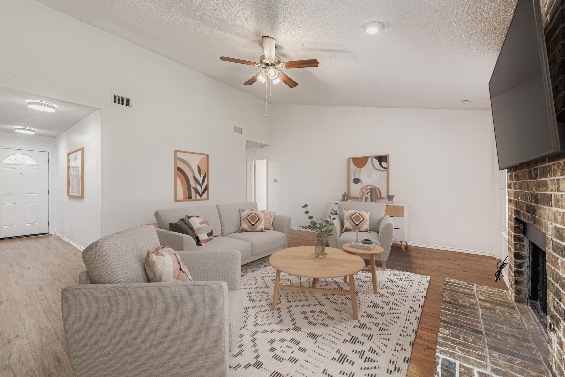 9839 Briar Ridge Drive Austin, TX 78748 - Photo 12 of 28 Living area with vaulted ceiling, a fireplace, wood finished floors, a textured ceiling, and ceiling fan