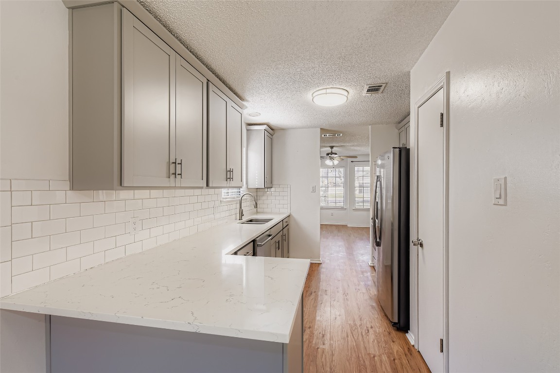 9839 Briar Ridge Drive Austin, TX 78748 - Photo 9 of 28 Kitchen featuring gray cabinetry, a textured ceiling, light stone counters, and decorative backsplash