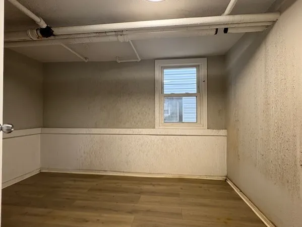 a view of an empty room with wooden floor and a window