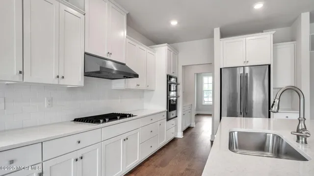 a kitchen with stainless steel appliances a sink dishwasher a refrigerator and white cabinets with wooden floor