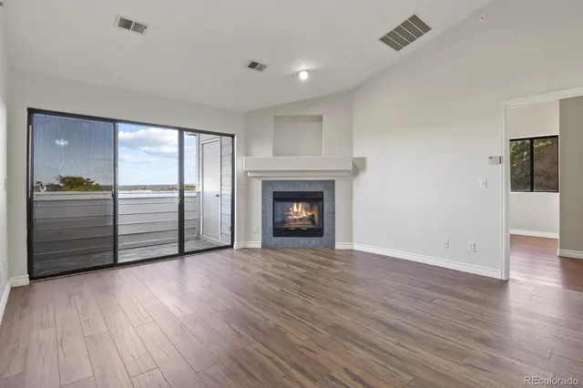 an empty room with wooden floor fireplace and windows