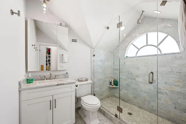 a bathroom with a toilet sink vanity granite and shower
